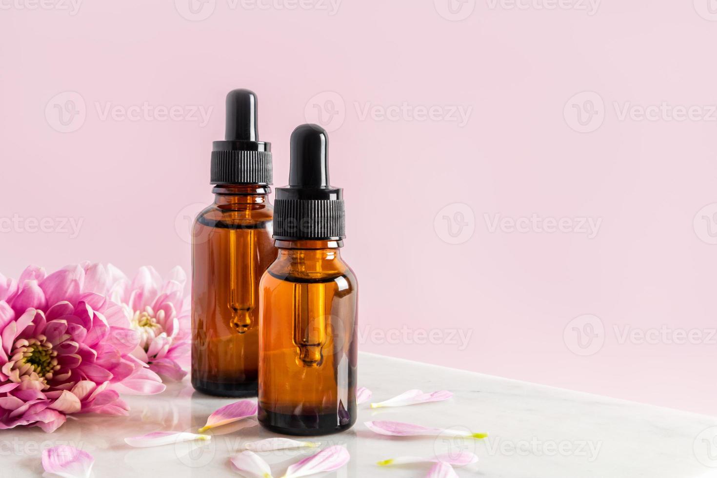 dois frascos de cosméticos com uma pipeta com soro para cuidados com a pele do rosto e do corpo ficam em um pódio de mármore com flores. fundo rosa. copie o espaço. foto