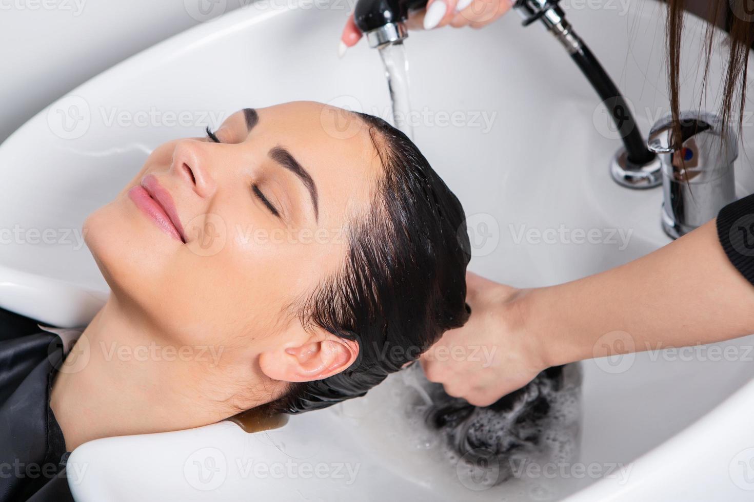 cabeleireiro profissional lavando cabelo de jovem no salão de beleza foto