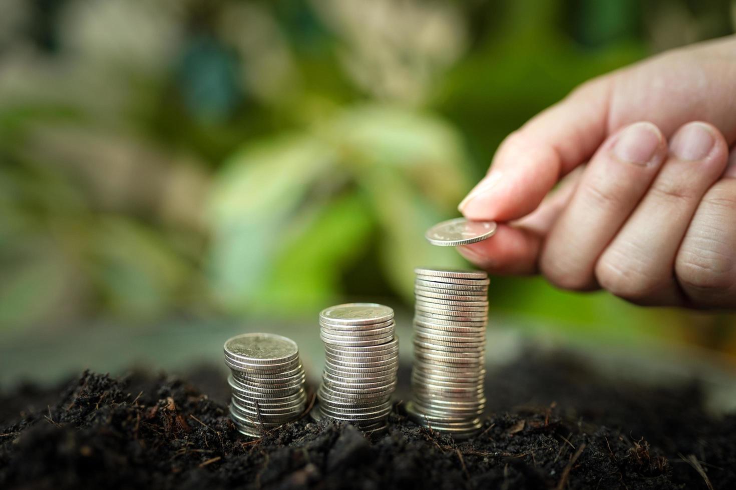 a mão da mulher está colocando moedas de prata na pilha de moedas de prata com fundo verde da natureza. economia de dinheiro e conceito de finanças de negócios, crescimento de negócios e futuro de dinheiro, sucesso financeiro foto