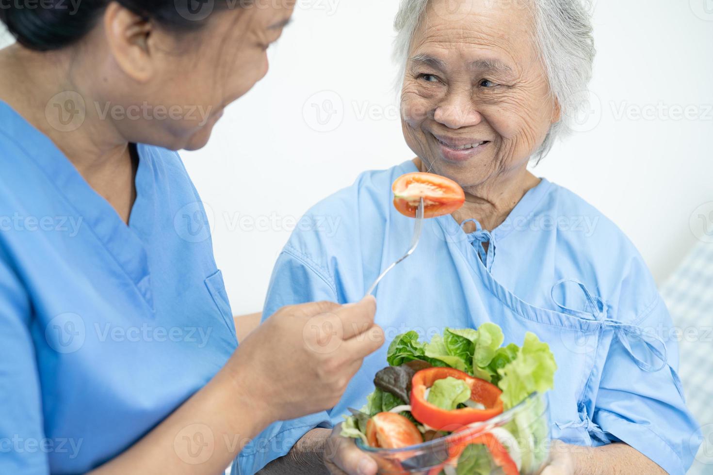 paciente asiático sênior ou idosa idosa comendo alimentos saudáveis de vegetais de café da manhã com esperança e feliz enquanto está sentado e com fome na cama no hospital. foto