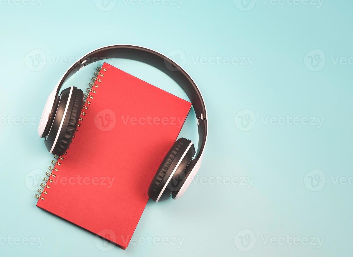 postura plana de caderno vermelho coberto com fones de ouvido em fundo azul com espaço de cópia. livro de áudio ou conceito de podcast. foto