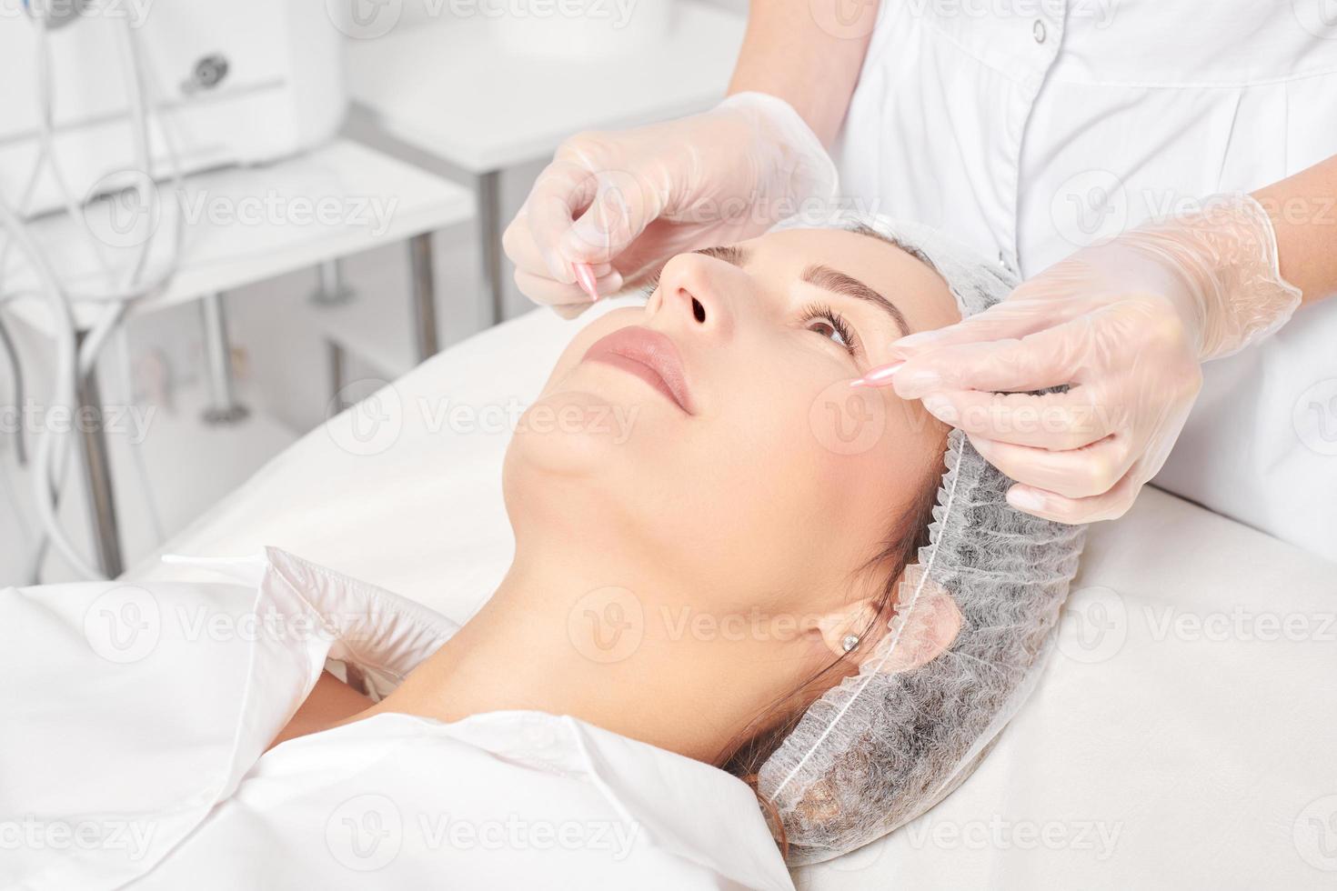 cosmetologista aplica cápsulas de óleo facial no rosto de mulher para rejuvenescimento, procedimento em salão de beleza foto