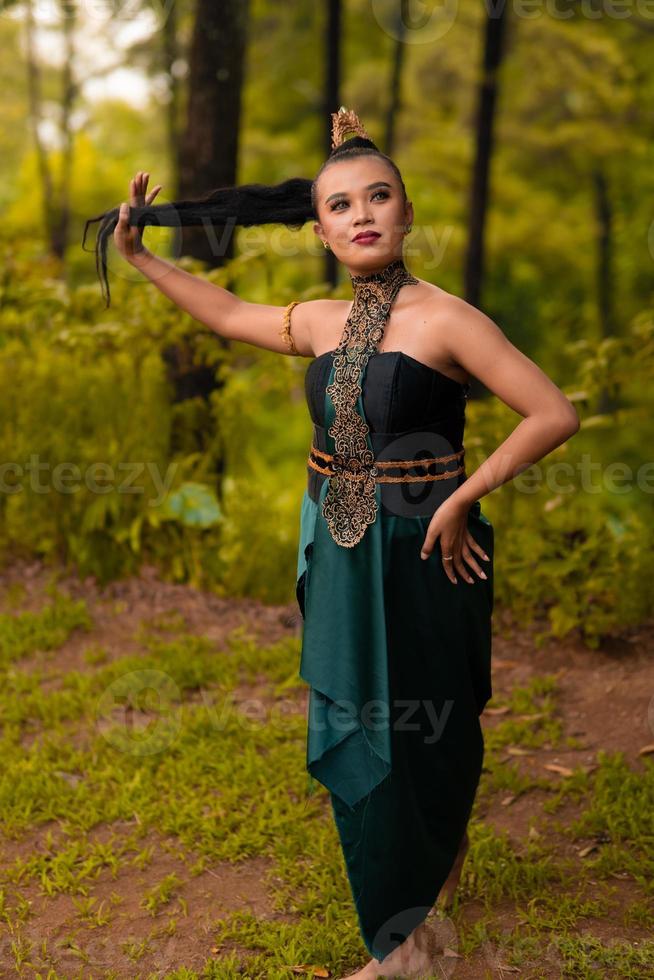 linda mulher asiática segurando seu cabelo preto em pé na frente da floresta em uma fantasia verde foto