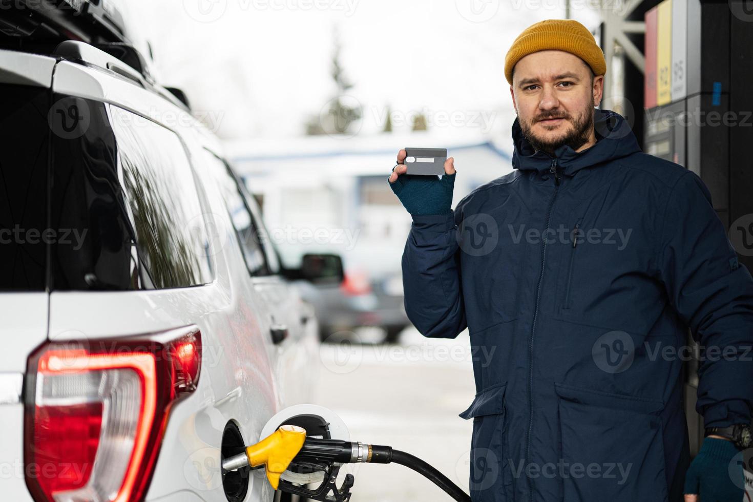 homem mostra cartão de crédito enquanto reabastece seu carro suv americano no posto de gasolina em clima frio. foto