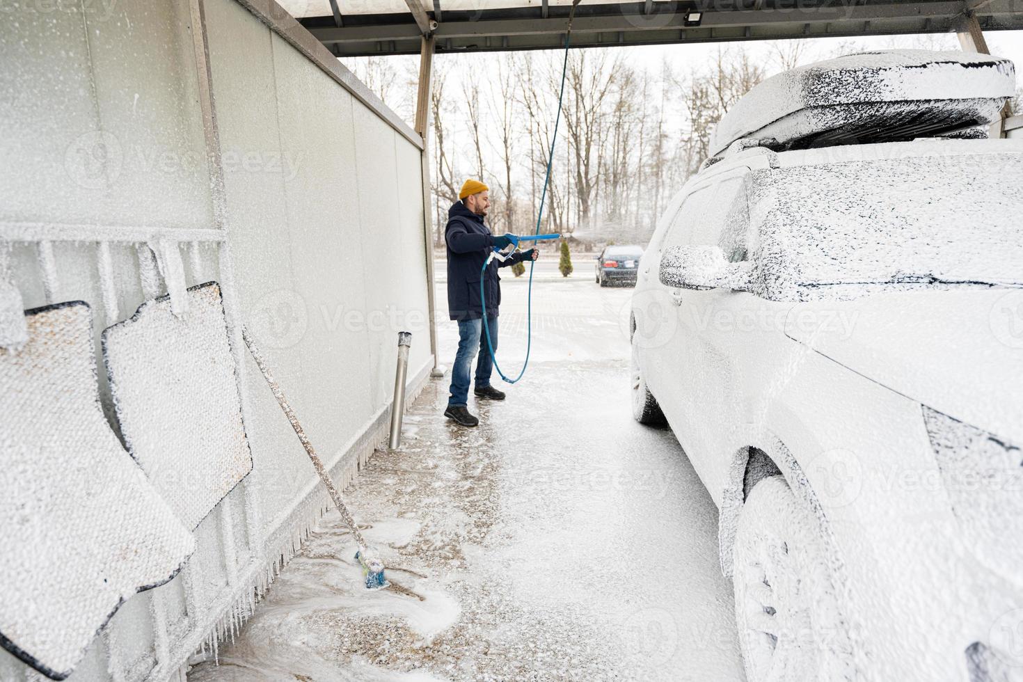 homem lavando carro suv americano com rack de teto em uma lavagem self-service em clima frio. foto