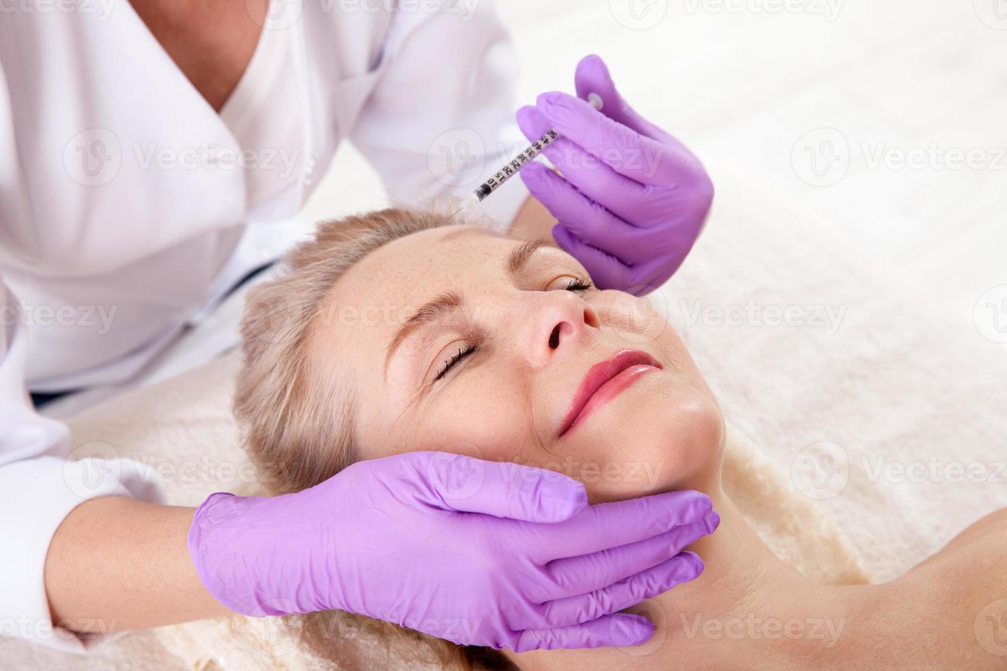 mulher de meia idade recebe injeção cosmética na testa. injeção de ácido hialurônico para procedimento de rejuvenescimento facial. mulher no salão de beleza. clínica de cirurgia plástica. foto