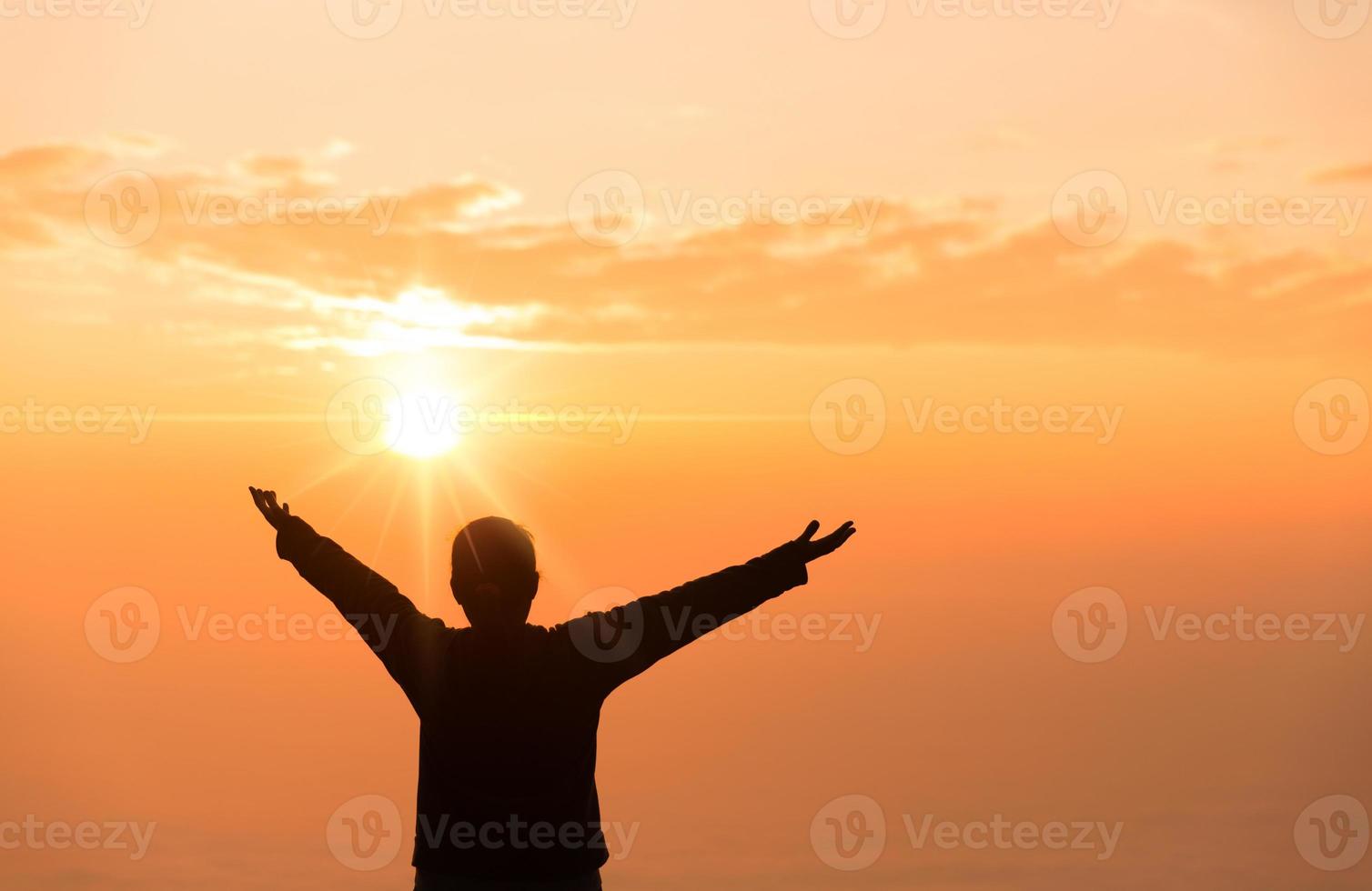 fé do conceito cristão. a oração espiritual entrega o brilho do sol com um belo fundo desfocado do pôr do sol. mãos femininas adoram a Deus com amor e fé. silhueta de uma mulher rezando com uma cruz. foto