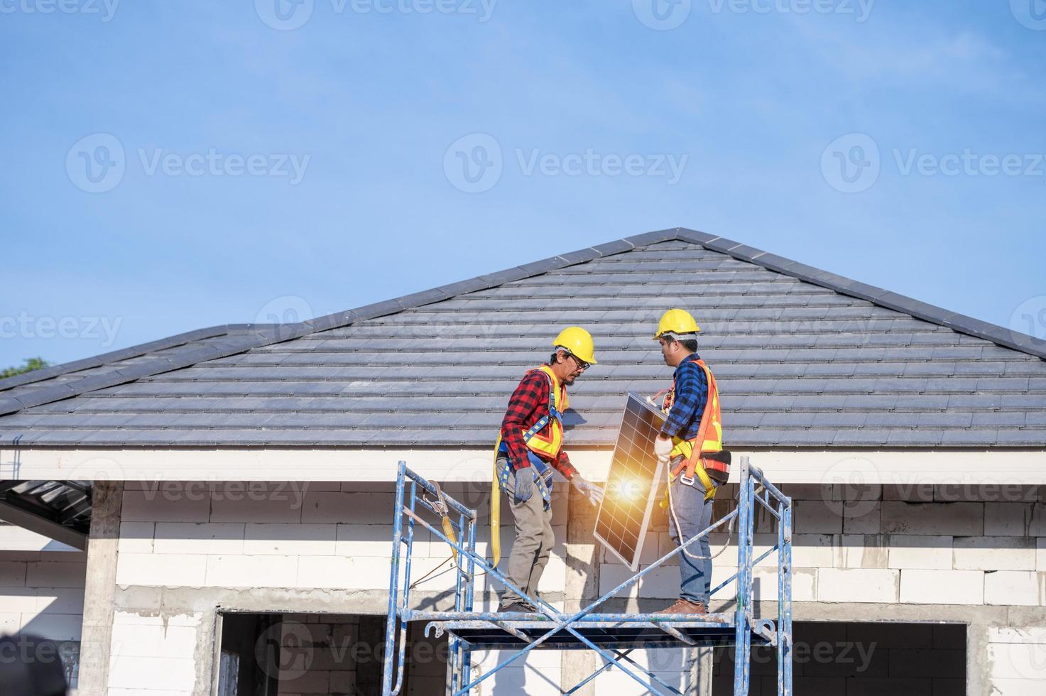 uma equipe de técnicos asiáticos instala painéis solares no telhado de uma casa. visão transversal do construtor no capacete instalando o conceito de sistema de painel solar de energia renovável foto