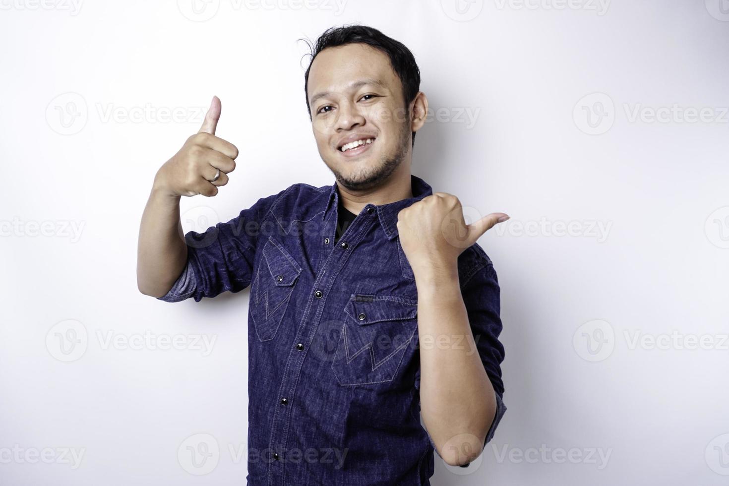 homem asiático animado vestindo camisa azul apontando para o espaço da cópia ao lado dele, isolado pelo fundo branco foto