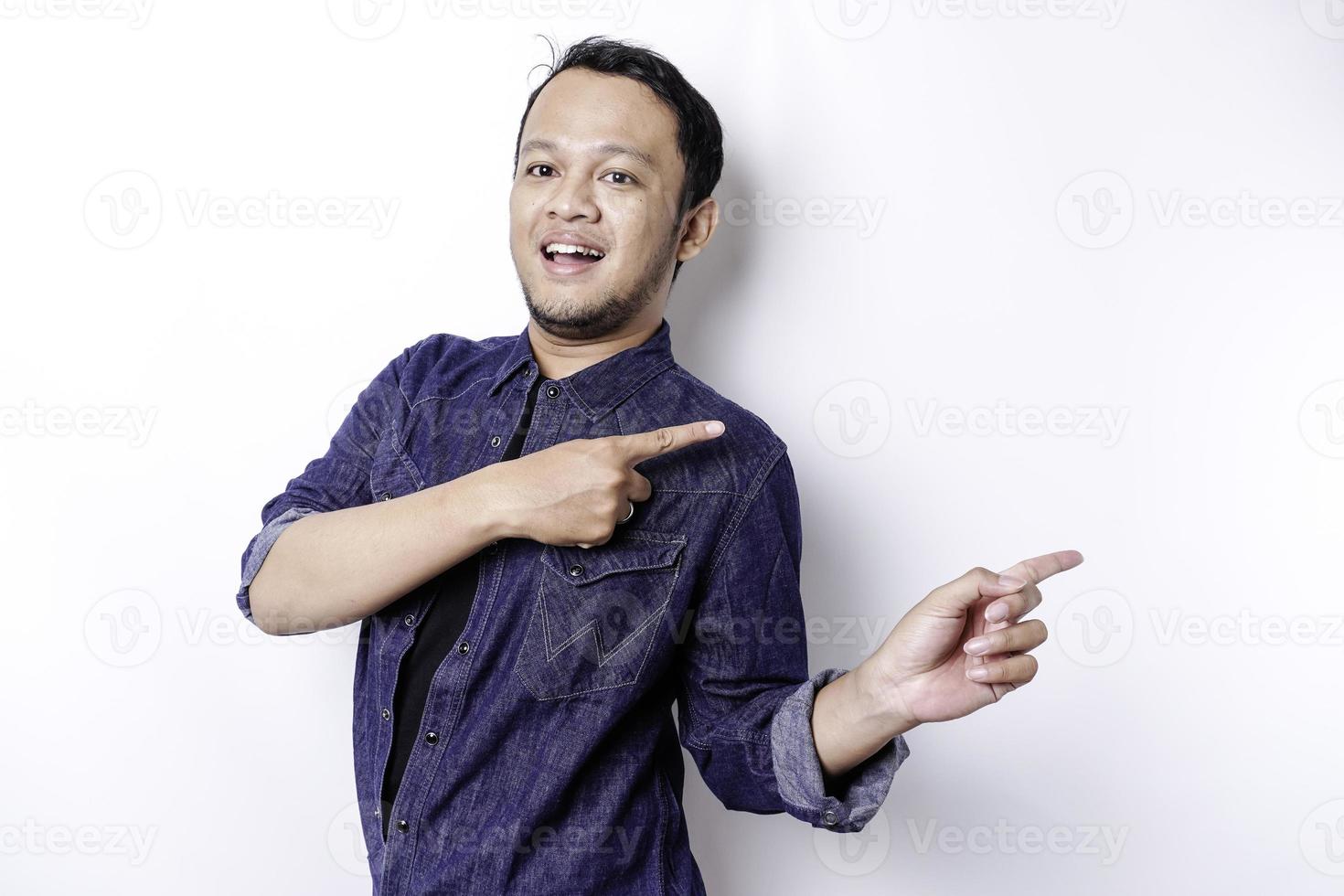 homem asiático animado vestindo camisa azul apontando para o espaço da cópia ao lado dele, isolado pelo fundo branco foto