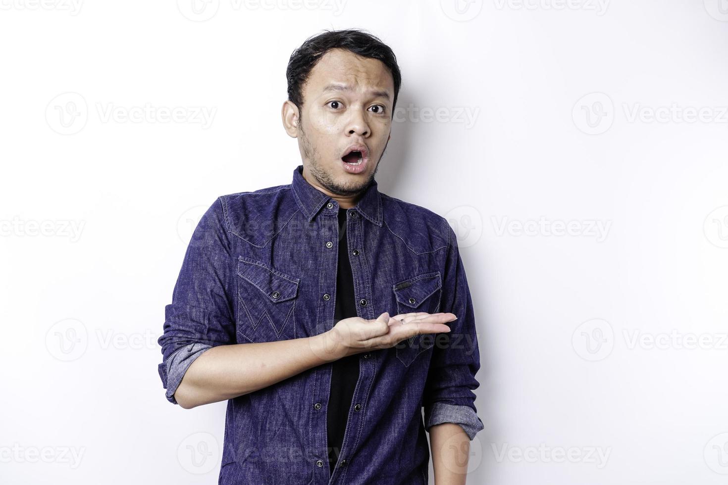 homem asiático chocado vestindo camisa azul apontando para o espaço da cópia ao lado dele, isolado pelo fundo branco foto