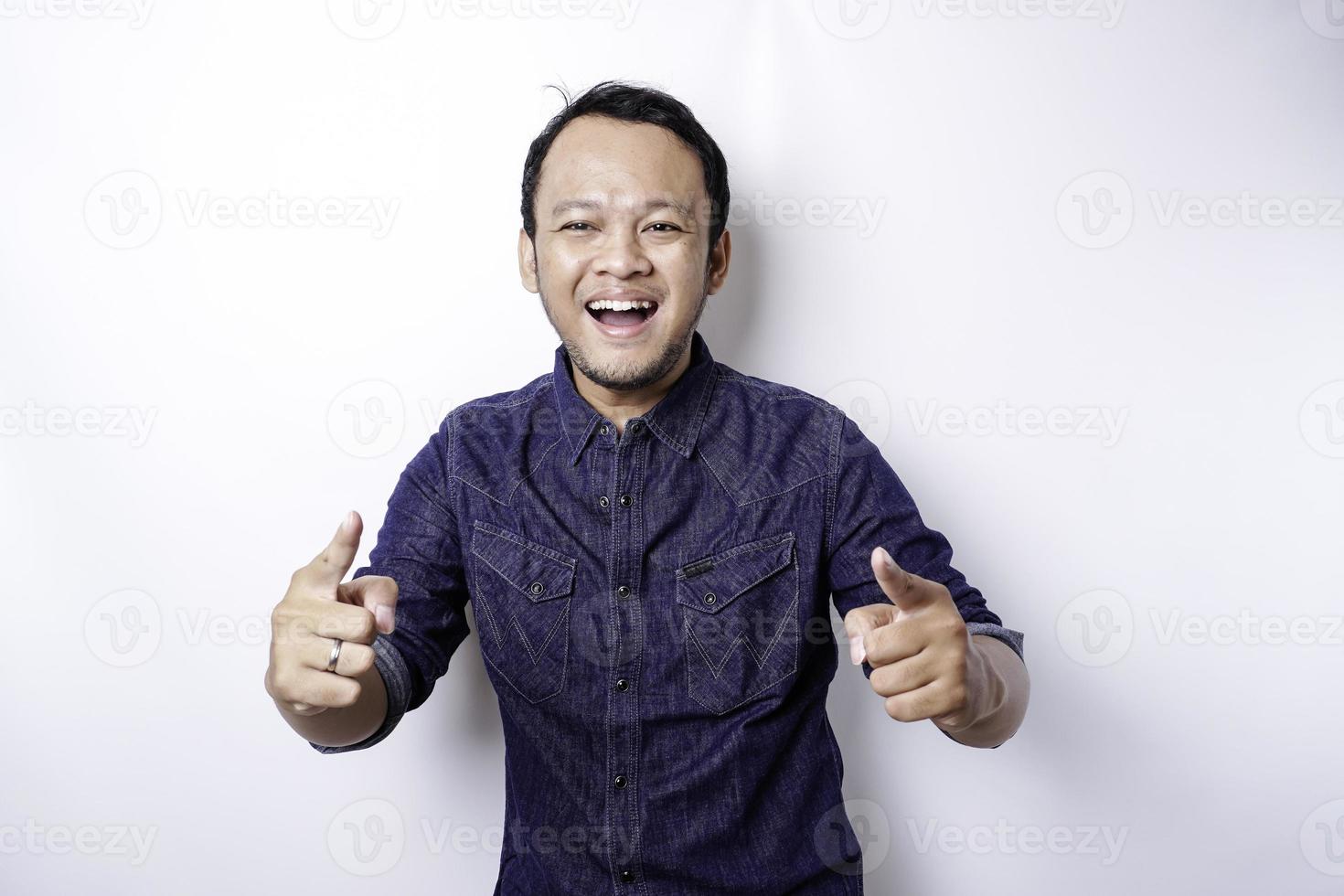 jovem asiático vestindo camisa azul em pé sobre fundo branco isolado, apontando o dedo para a câmera com cara feliz. boas energias e vibrações. foto