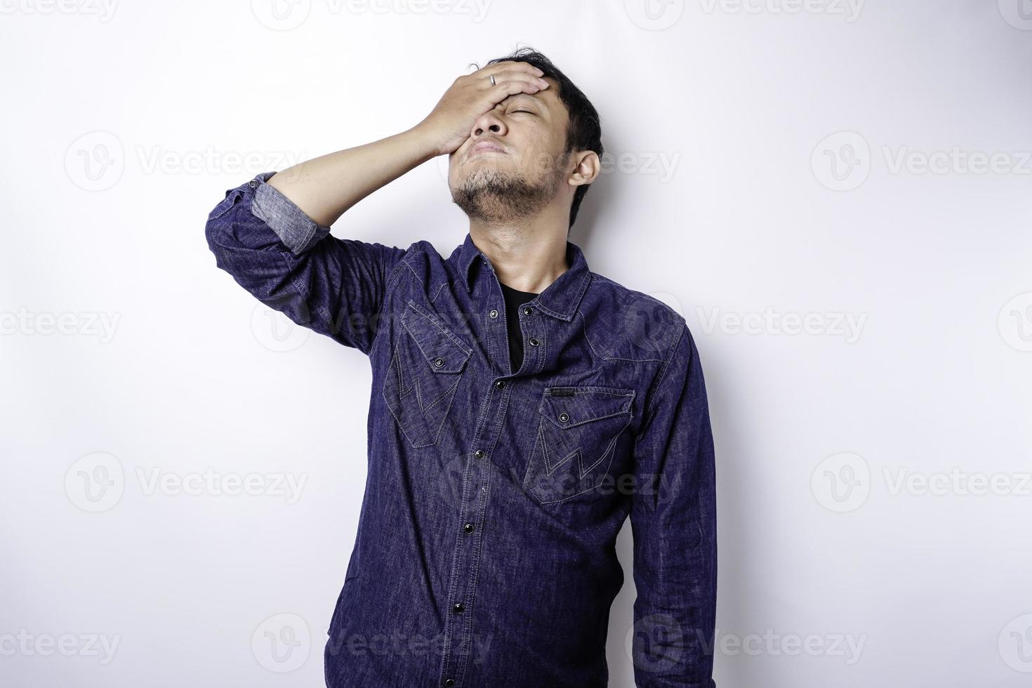 um retrato de um homem asiático vestindo uma camisa azul isolada por um fundo branco parece deprimido foto