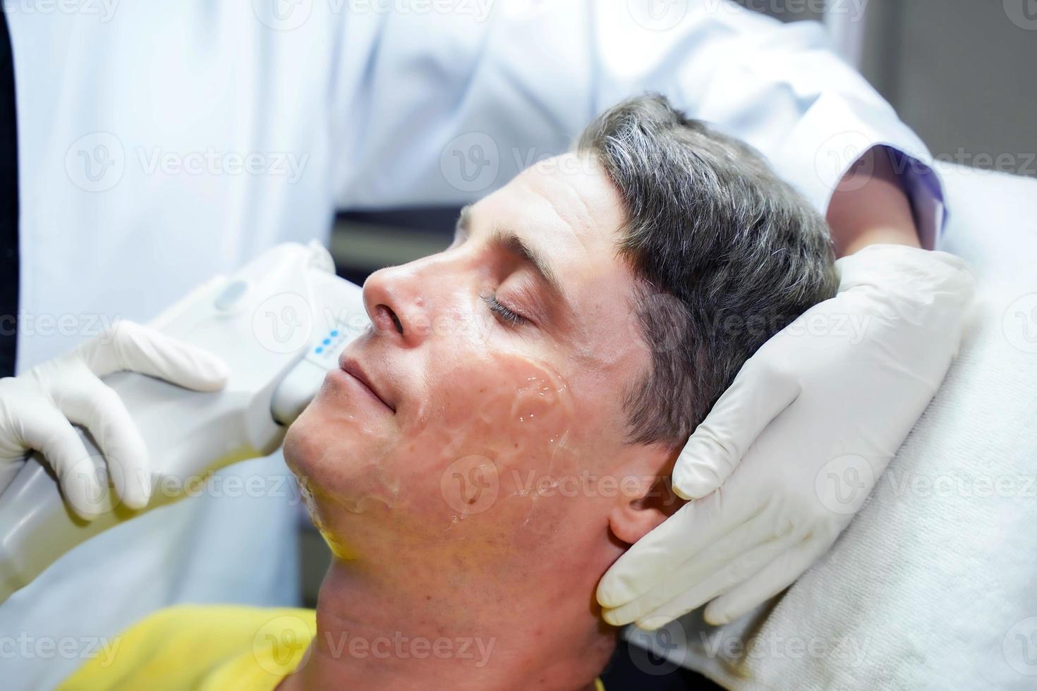 homem bonito closeup tendo terapia de luz colorida para estimular a pele facial pelo bem-estar cosmetologista profissional. foto