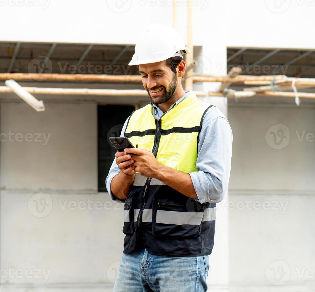 arquiteto ou engenheiro masculino usando telefone celular para comunicação enquanto trabalhava no canteiro de obras. empreiteiro profissional em pé no local de desenvolvimento habitacional usa smartphone no trabalho. foto