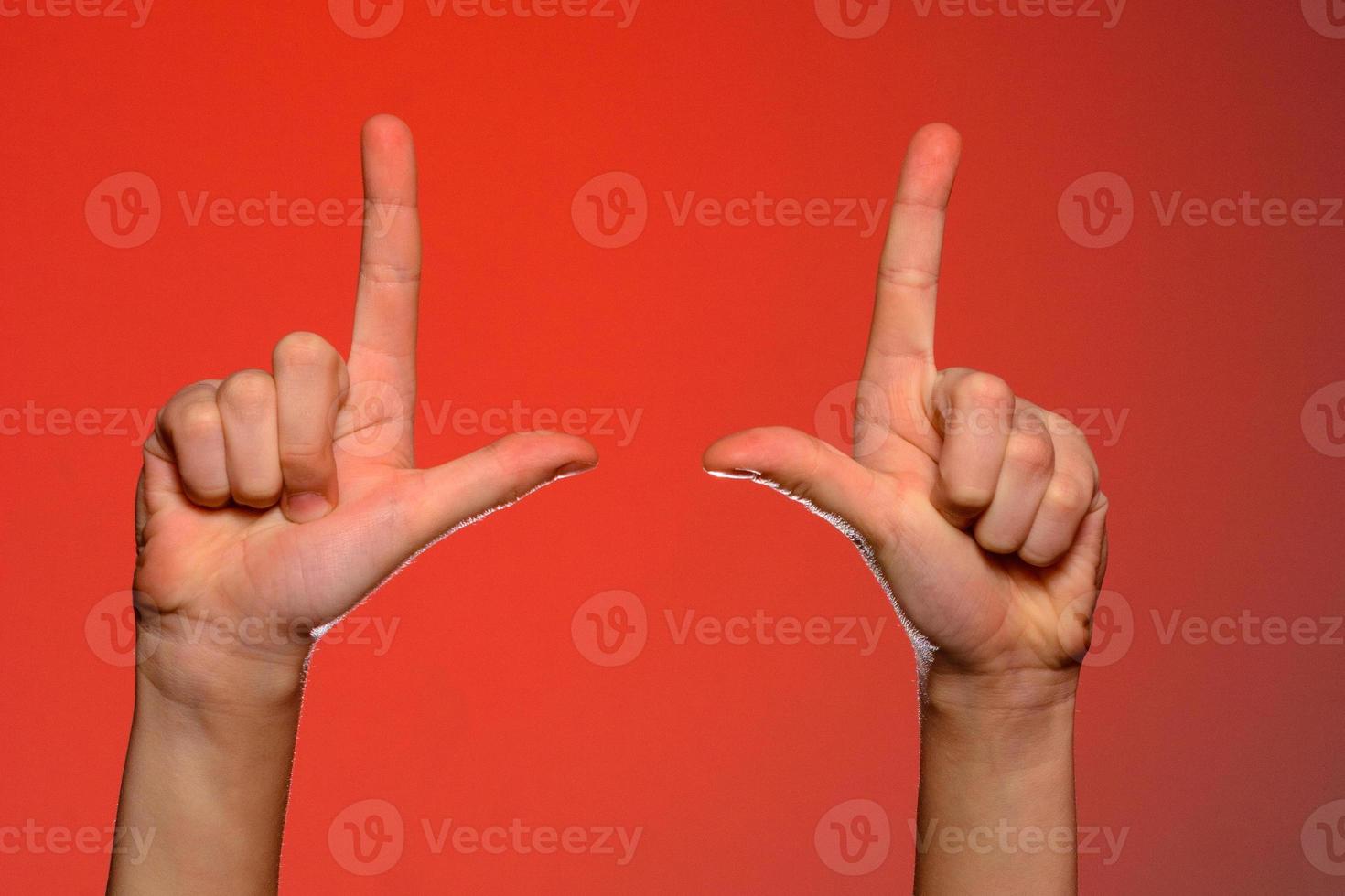 mão humana com dedos dobrados, mostra um dedo indicador que simboliza uma pistola, isolada em um fundo vermelho foto