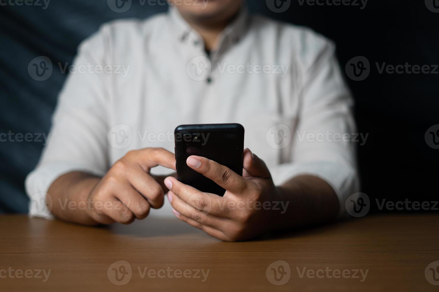 homem de negócios segurando um smartphone e rolando em uma mesa de madeira foto