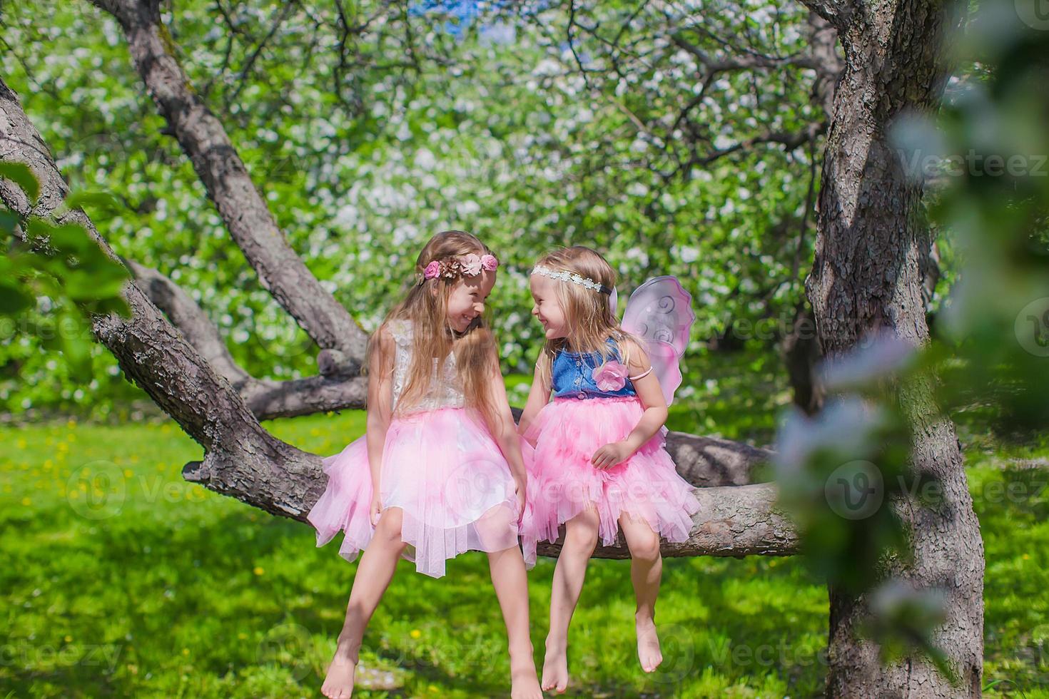 meninas adoráveis sentadas na árvore florescendo no jardim de maçã foto