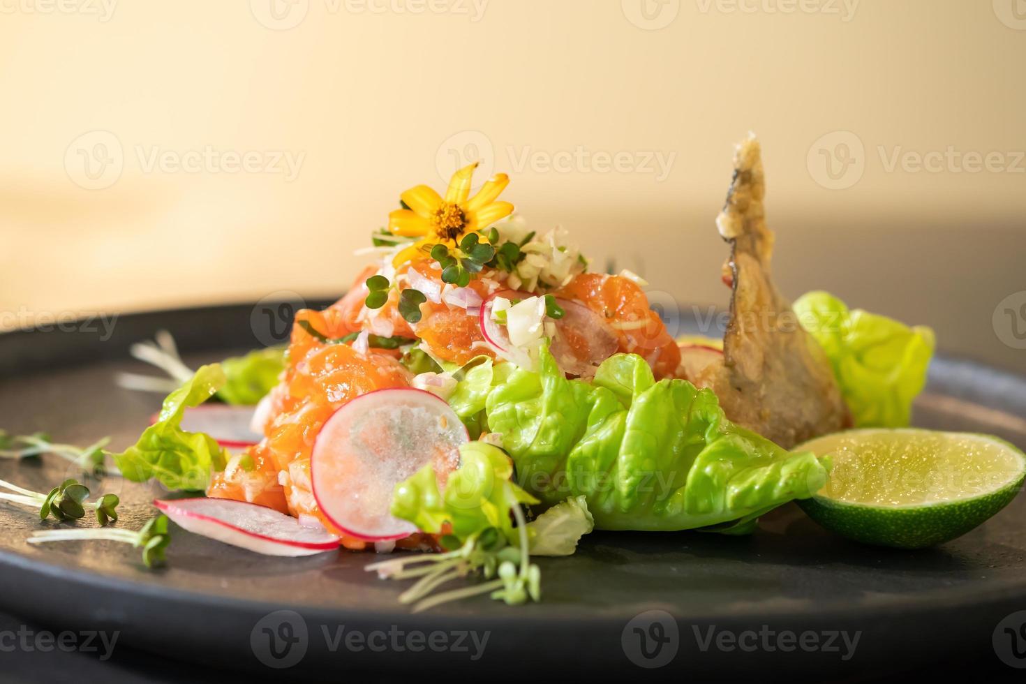 feche o estilo de comida tailandesa de salada de salmão cru picante decorado com pele de peixe frito crocante e flor amarela no topo e micro erva ao redor do prato. pronto para servir e comer. foto