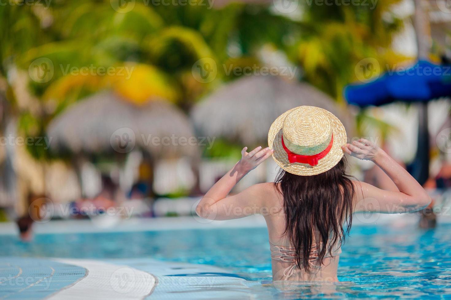 bela jovem relaxante na piscina. vista traseira da garota na piscina ao ar livre no hotel de luxo foto