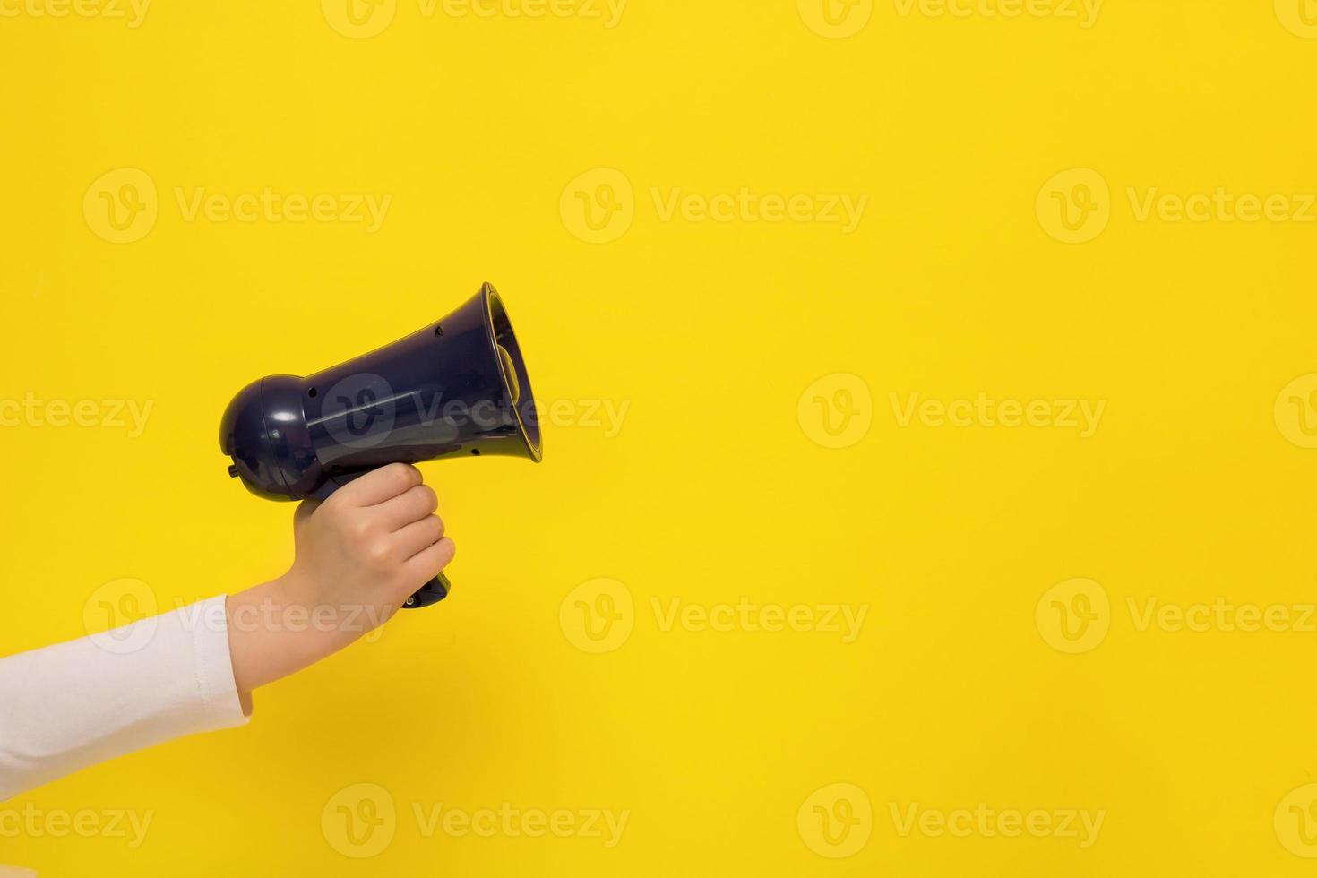 mão infantil segurando um megafone em um fundo amarelo com espaço de cópia foto