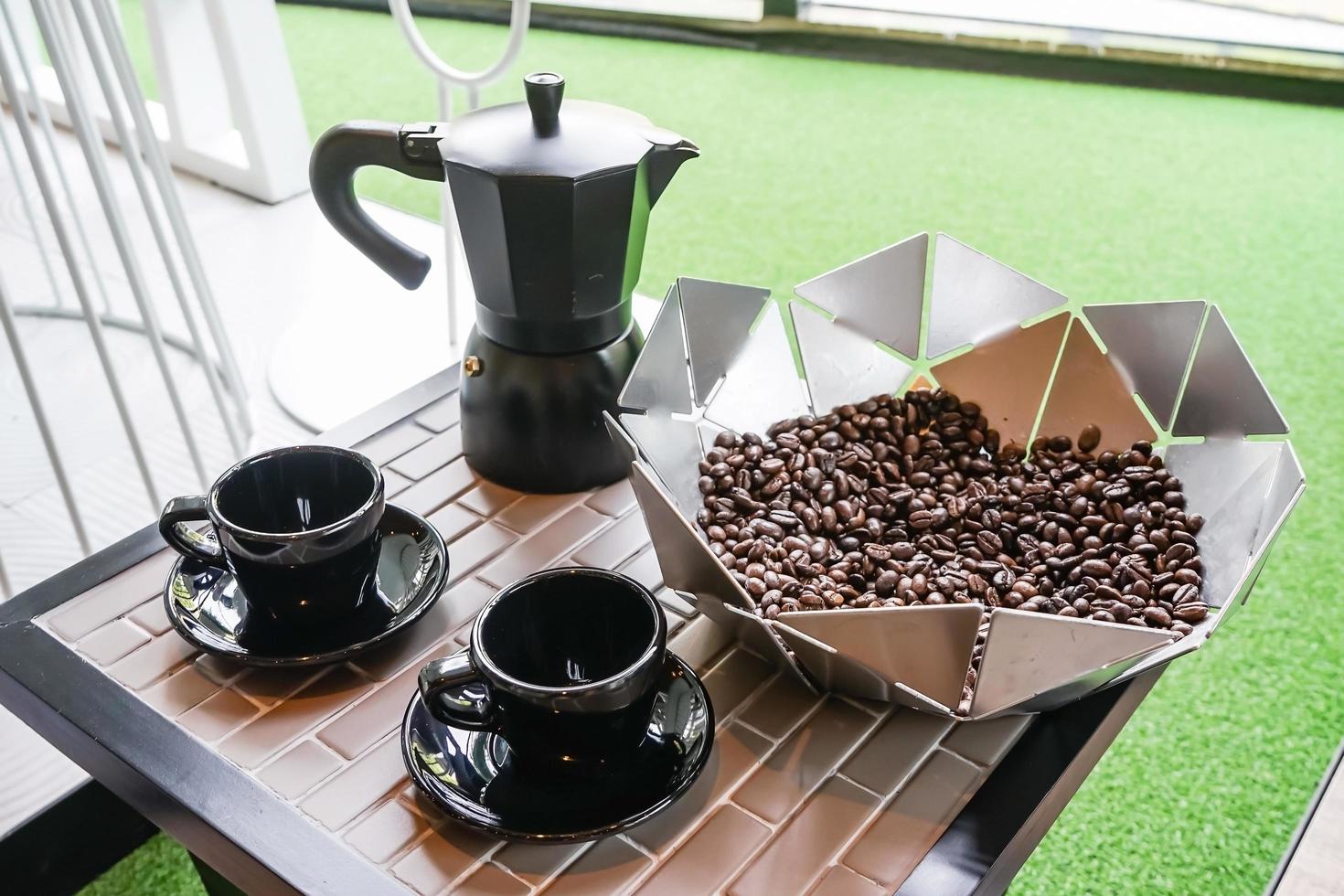 cafeteira metálica italiana com grãos de café e xícara de café preto na mesa de madeira. cafeteira mocha para fazer café expresso foto