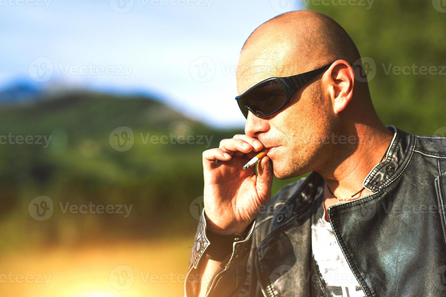 homem com óculos e jaqueta preta fumando cigarro foto