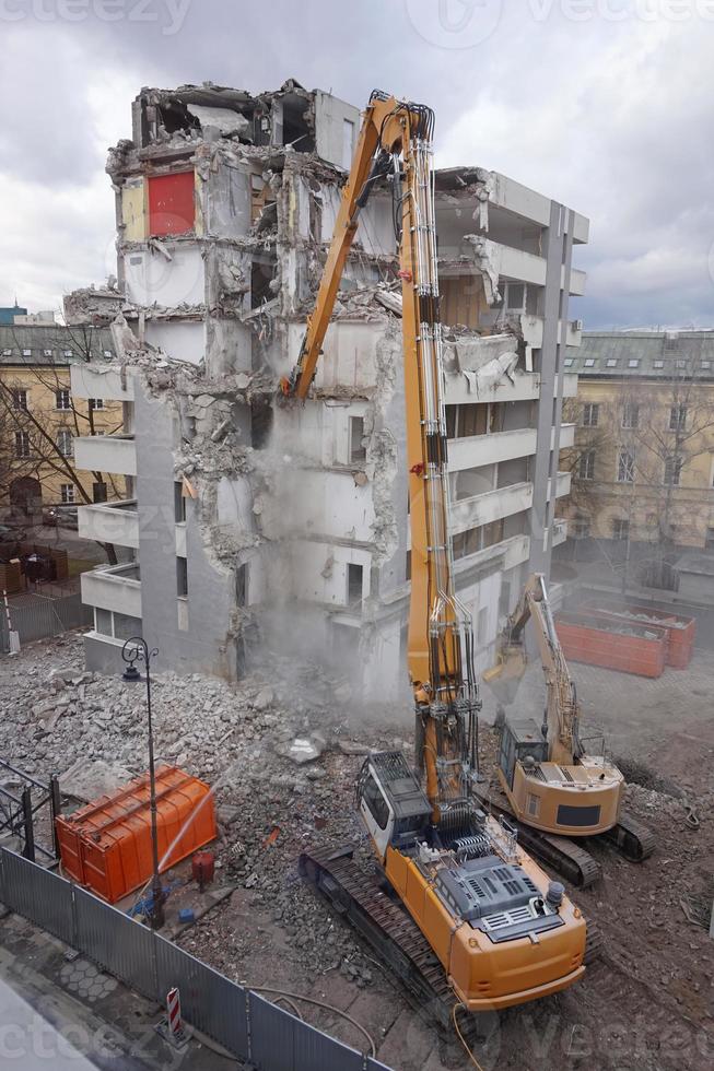 máquina de demolição e desmontagem em ação com edifício de vários andares foto