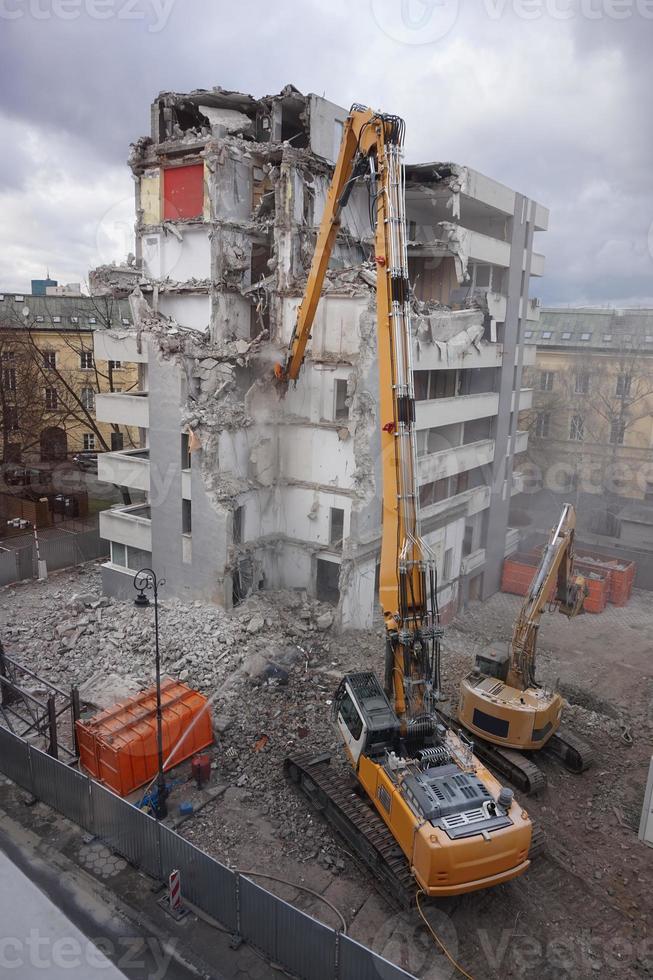 máquina de demolição e desmontagem em ação com edifício de vários andares foto