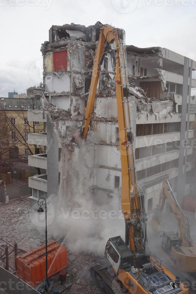 máquina de demolição e desmontagem em ação com edifício de vários andares foto