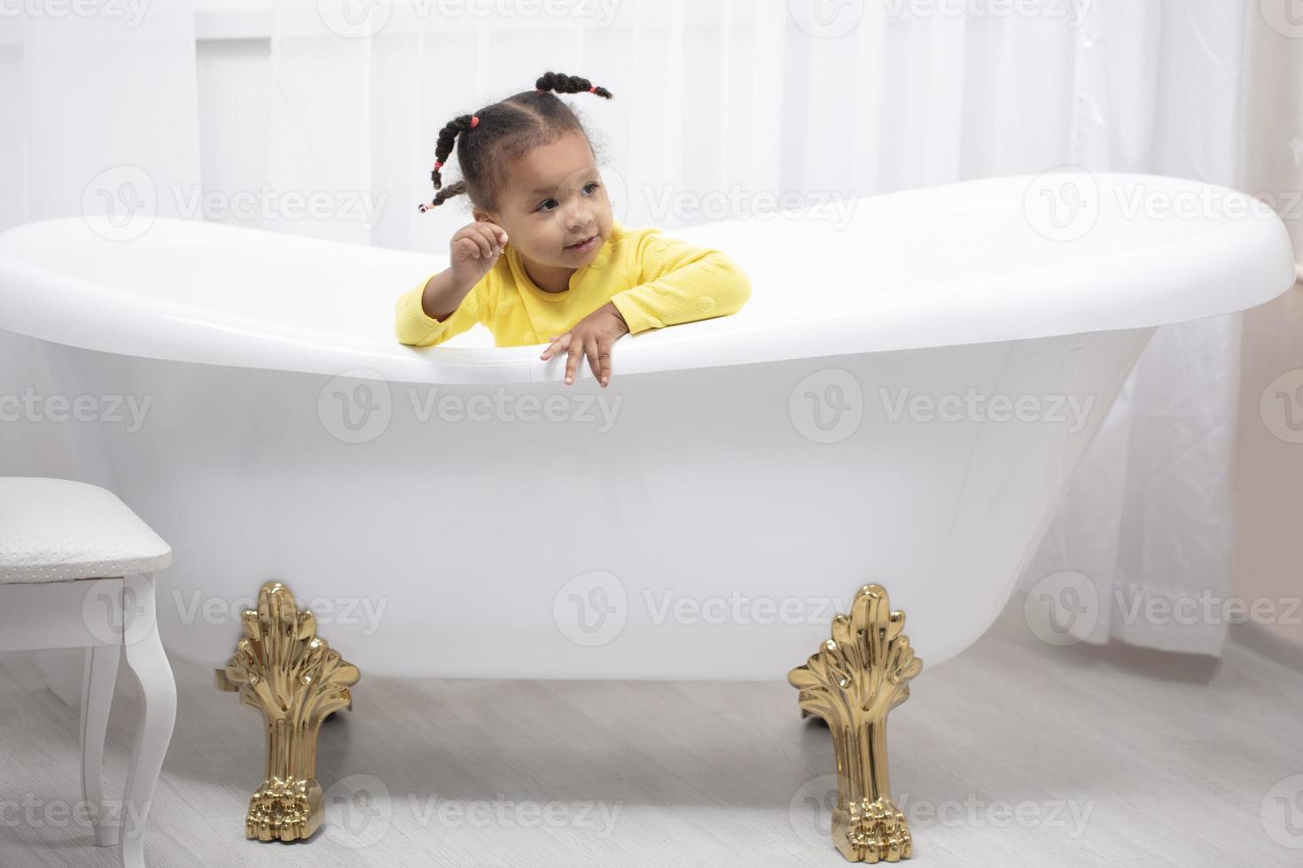 menina afro-americana em um vestido amarelo com tranças encaracoladas senta-se em um banho retrô. foto