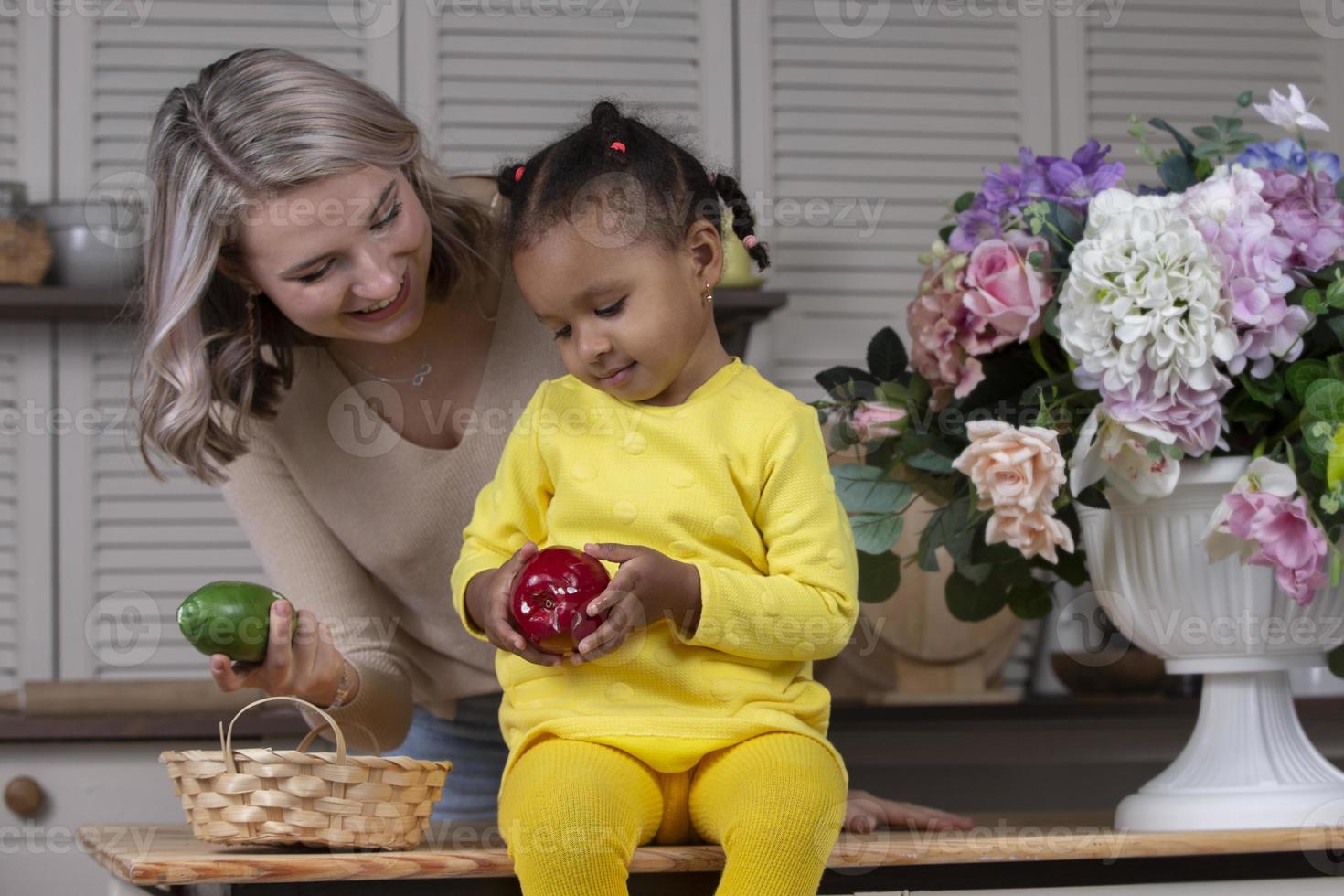 mãe e filha multiétnicas brincam em casa na cozinha. mãe alegre com filha de nacionalidade africana. família de diferentes raças. foto