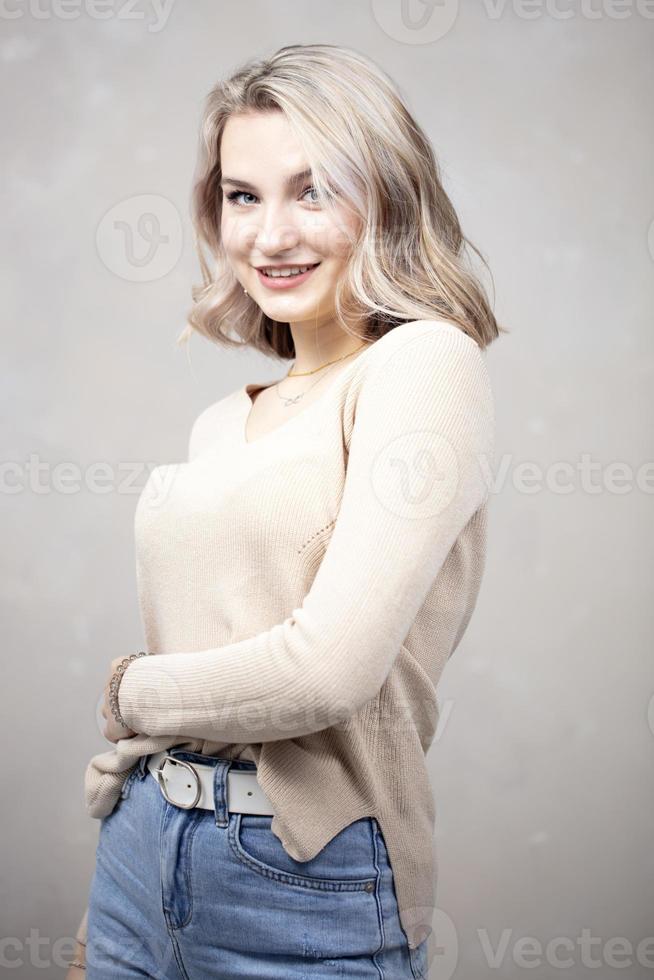 uma linda jovem com cabelos loiros e olhos azuis olha para a câmera e sorri. a menina tem dezessete anos. foto