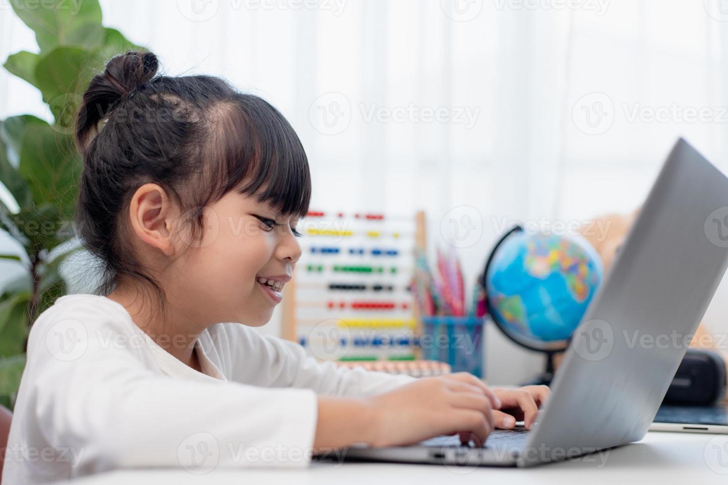 colegial asiática fazendo sua lição de casa com o laptop em casa. as crianças usam aparelhos para estudar. educação e ensino a distância para crianças. educação domiciliar durante a quarentena. ficar em casa foto