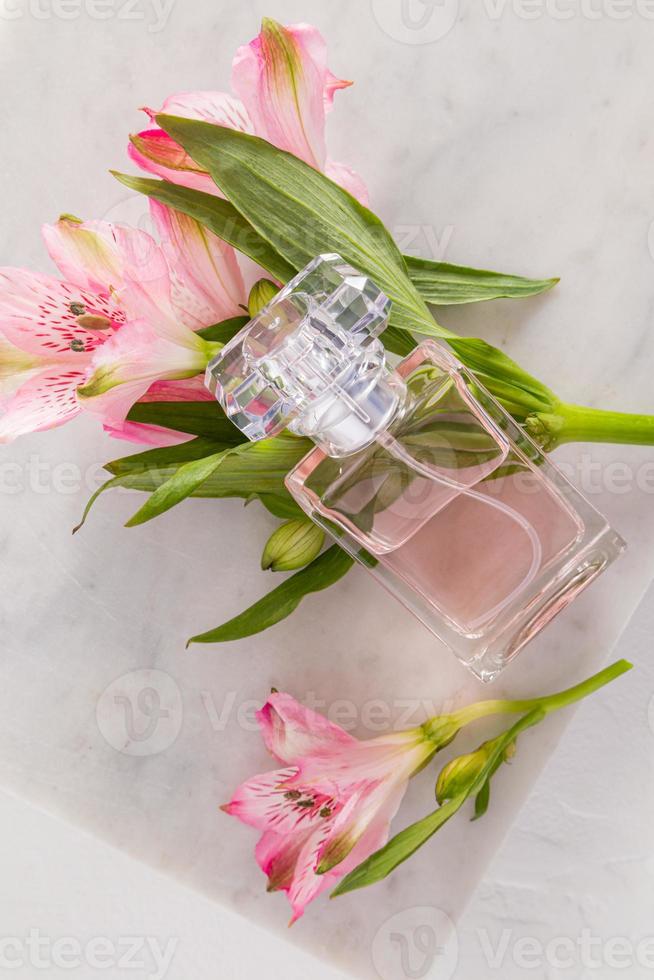 um frasco de perfume feminino ou água de toalete fica sobre as flores rosa da primavera. apresentação e divulgação de uma delicada fragrância floral. visão vertical. foto