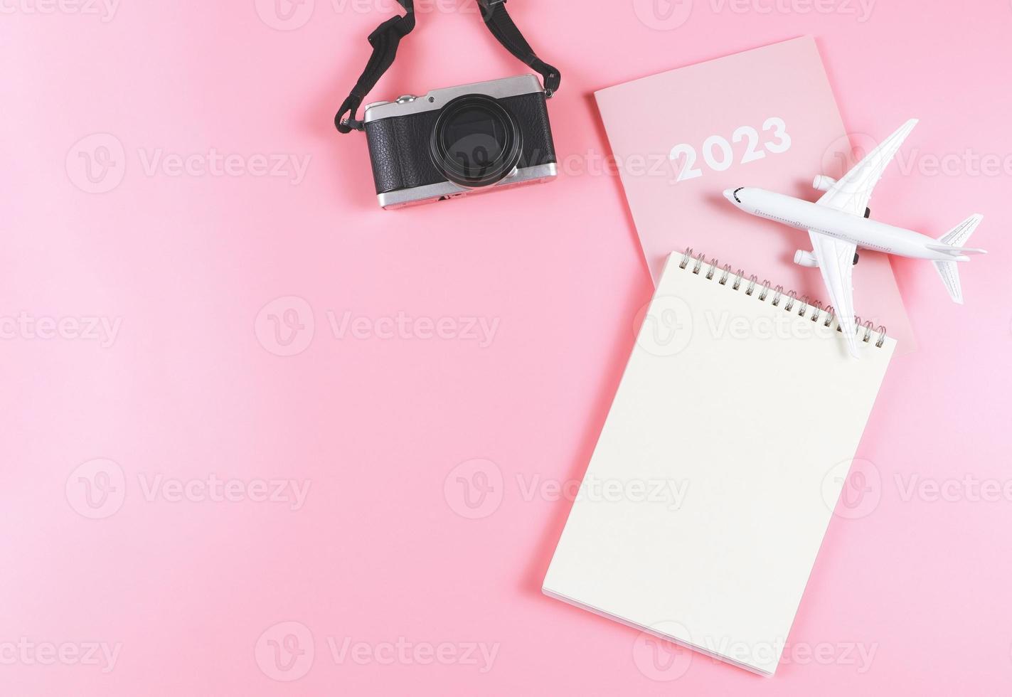 configuração plana de caderno de papel em branco no diário rosa 2023 com modelo de avião e câmera em fundo rosa. conceito de plano de viagem. foto