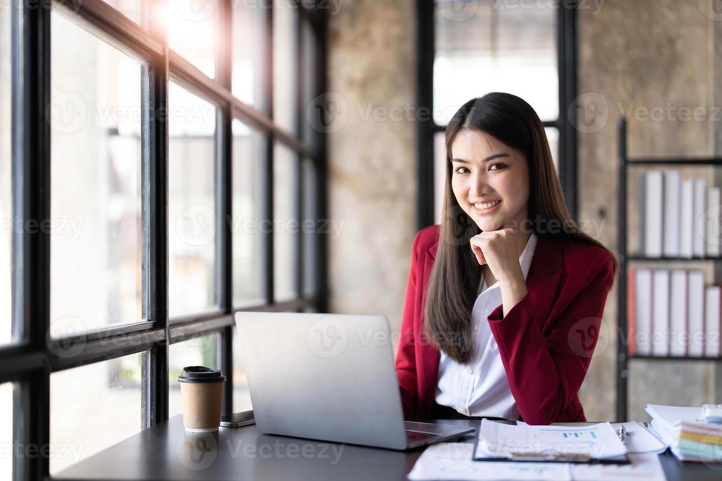 sorria linda mulher asiática de negócios está trabalhando em um computador portátil em um escritório moderno. fazendo relatório de análise contábil dados de investimento imobiliário, conceito de sistemas financeiros e tributários foto