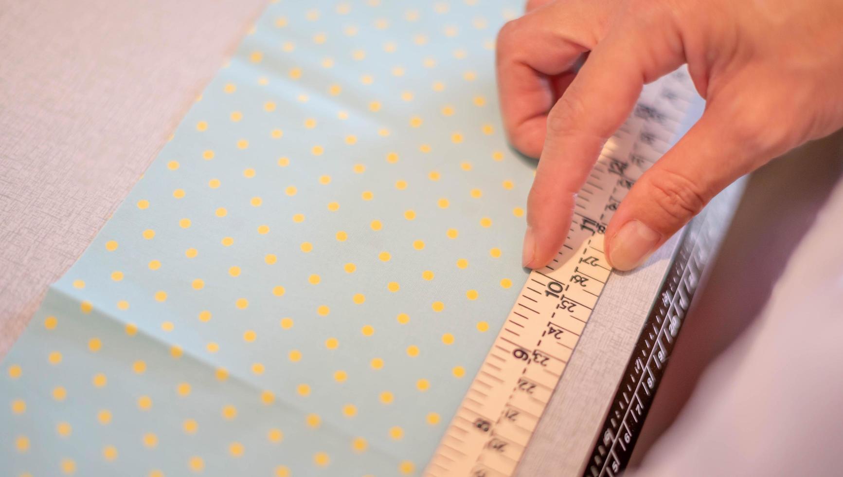 mãos femininas de designer no trabalho com close-up de tecido. alfaiate medindo a quantidade necessária de material para costurar pano. foto