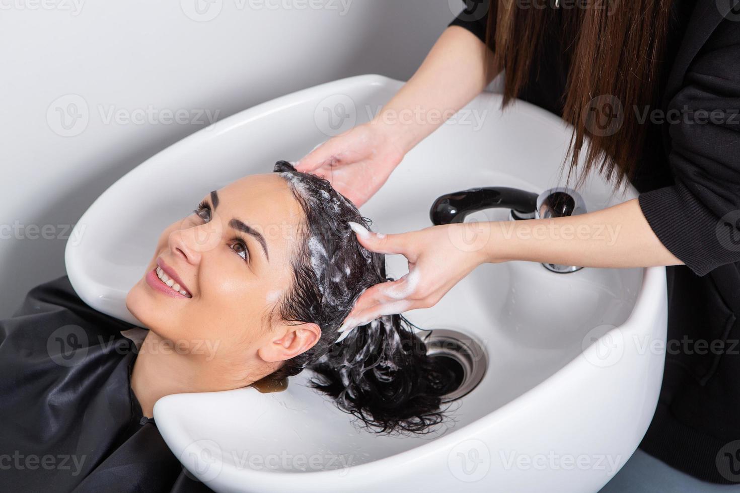 cabeleireiro profissional lavando cabelo de jovem no salão de beleza foto