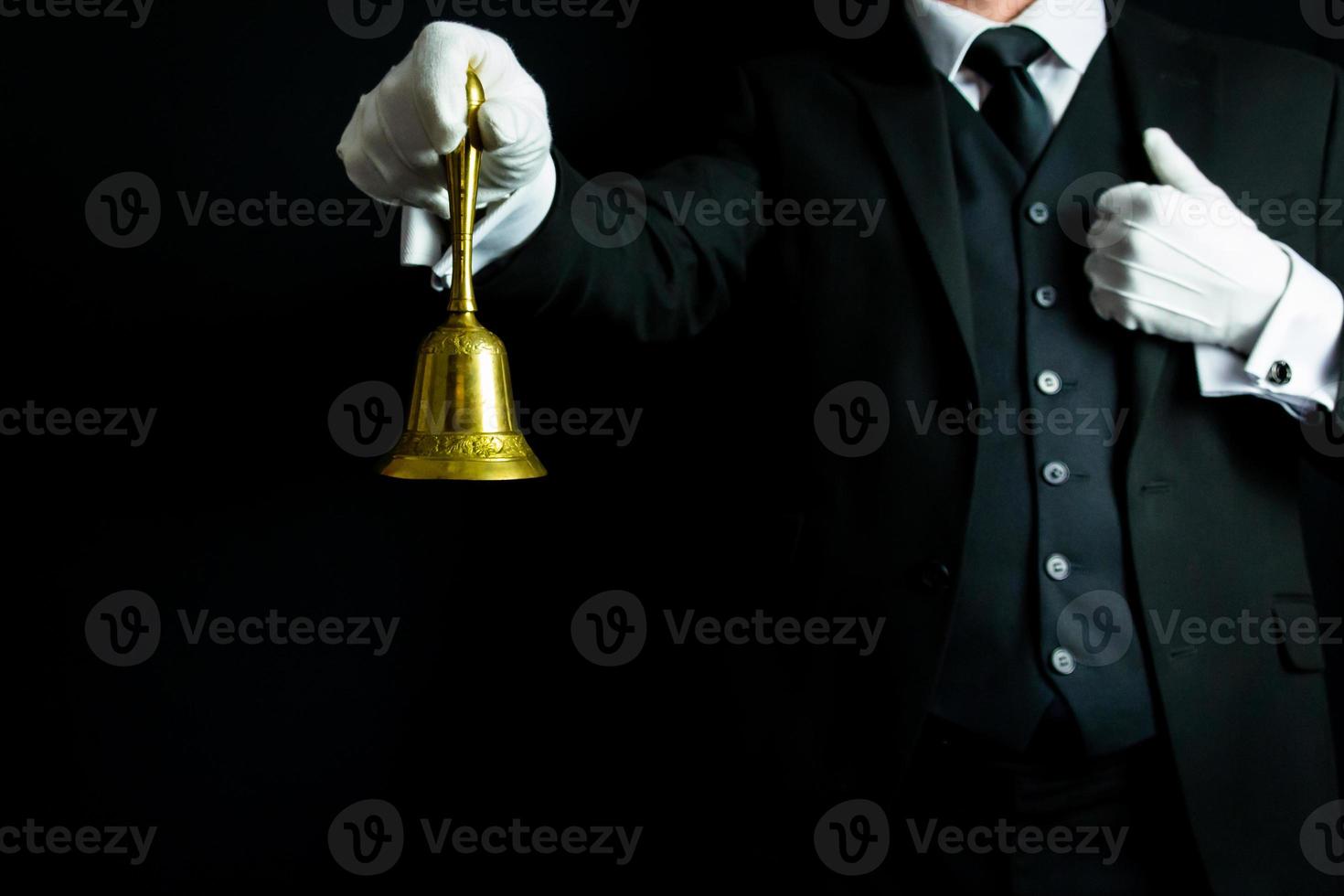 retrato de mordomo ou garçom em terno preto e luvas brancas segurando o sino de ouro. anel para o conceito de serviço. foto