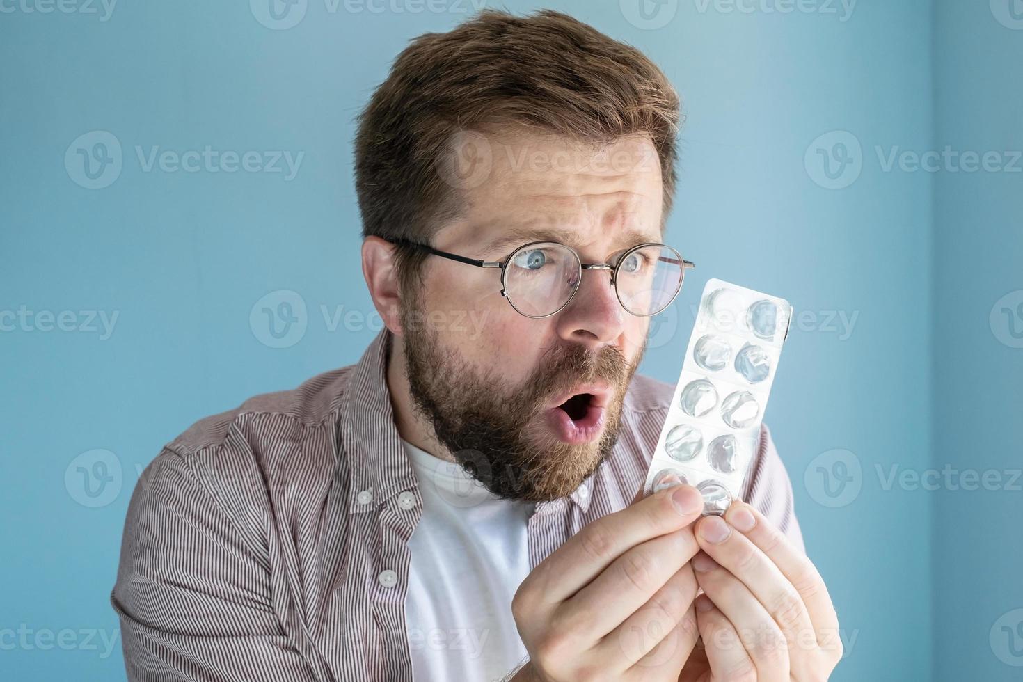 homem olha para um pacote de remédio vazio com apenas um comprimido sobrando, ele fica chocado e perplexo. foto