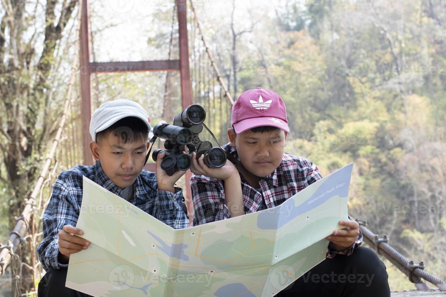 meninos adolescentes asiáticos seguram o mapa do parque nacional, lendo detalhes da observação de pássaros antes de usar seus binóculos para observar o pássaro que está sentado em brunches e voando no céu, conceito de férias de verão. foto