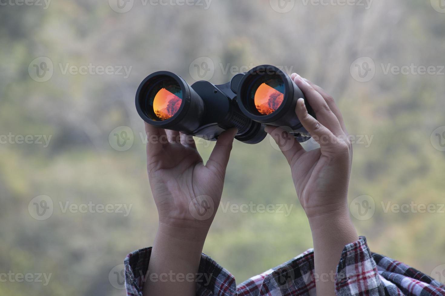 mãos segurando binóculos, fundo natural desfocado, conceito para férias, observação, trekking, camping, caminhadas e observação de pássaros. foto