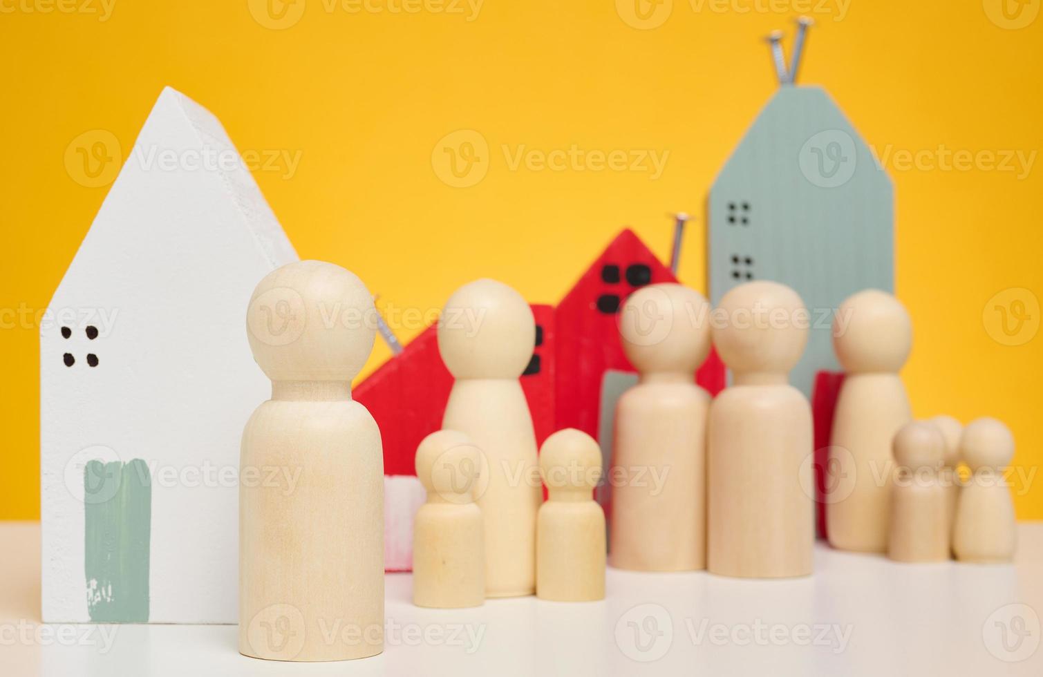 casa de madeira e estatuetas em miniatura de uma família e um corretor de imóveis em um fundo amarelo. o conceito de venda e compra de imóveis, investimento foto