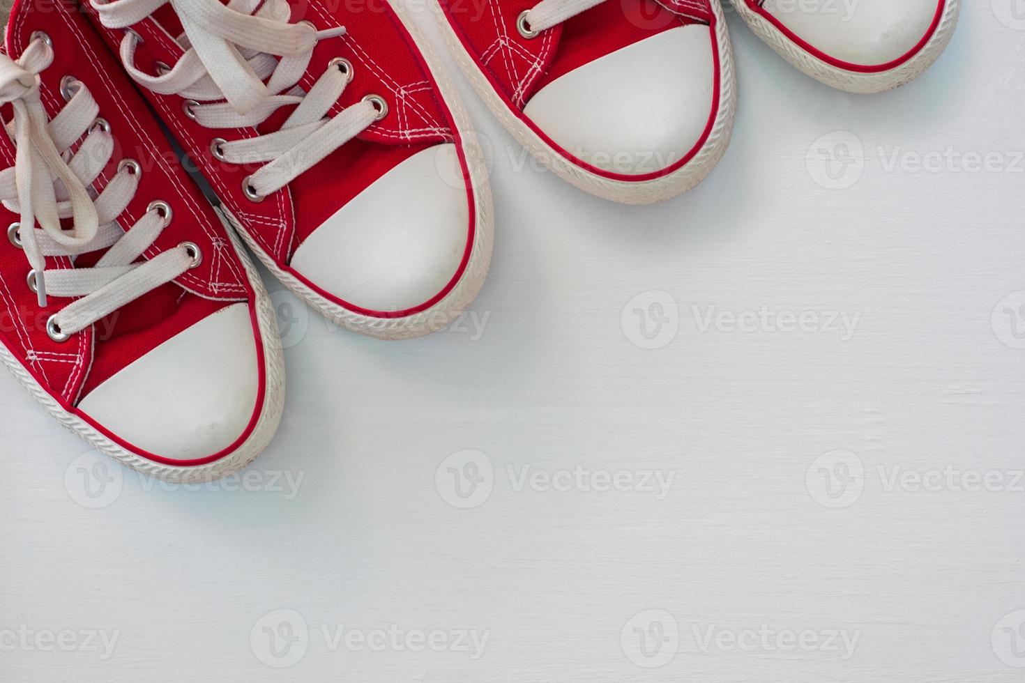 dois pares de tênis vermelhos jovens em uma superfície de madeira branca foto