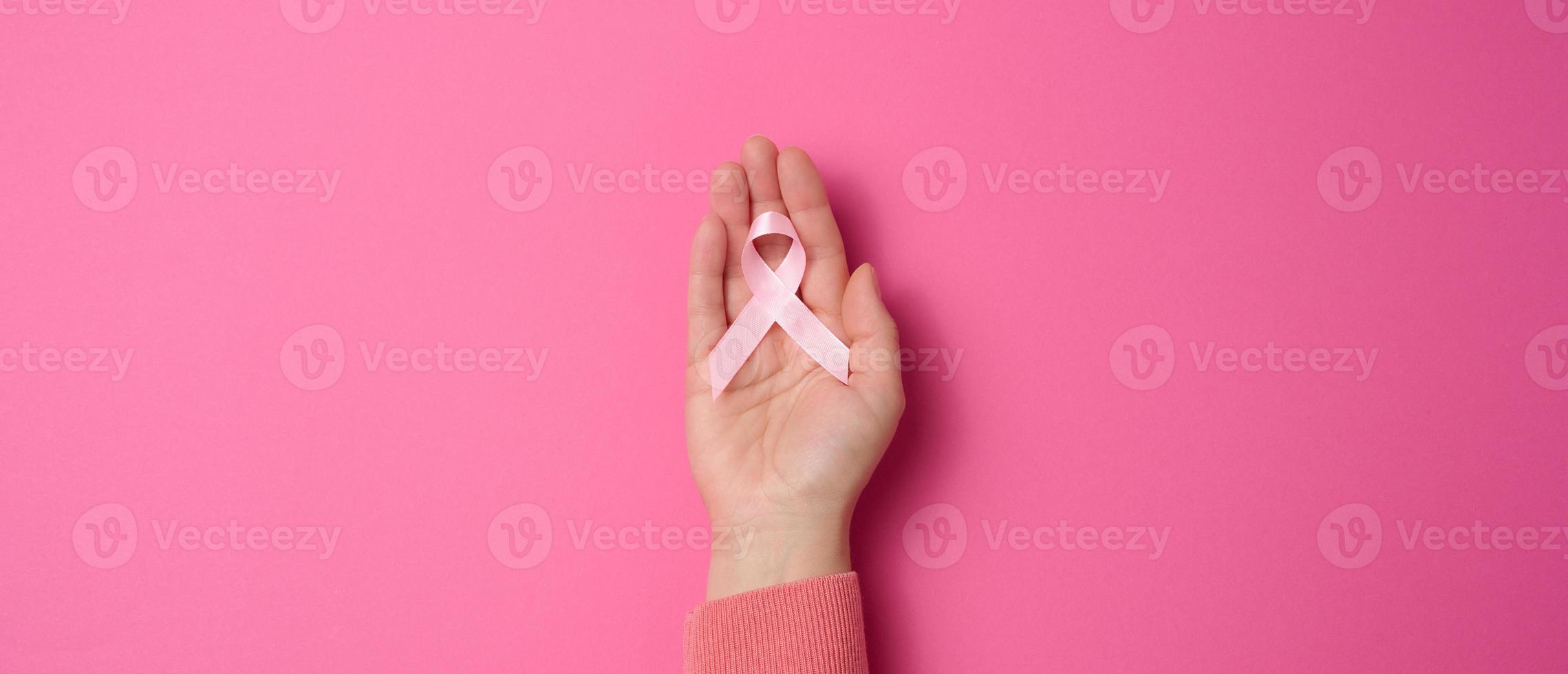 mão feminina segura uma fita de seda rosa na forma de um laço em um fundo rosa. símbolo da luta contra o câncer de mama foto