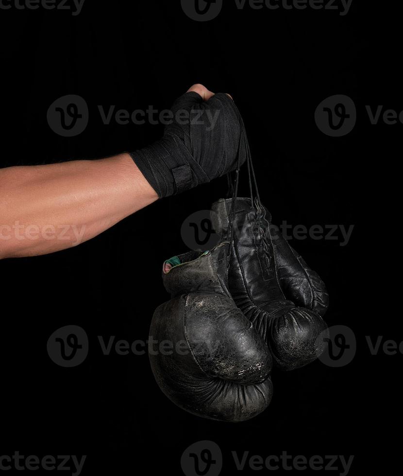 braço envolto em uma bandagem esportiva elástica preta segura um par de luvas de boxe de couro vintage foto