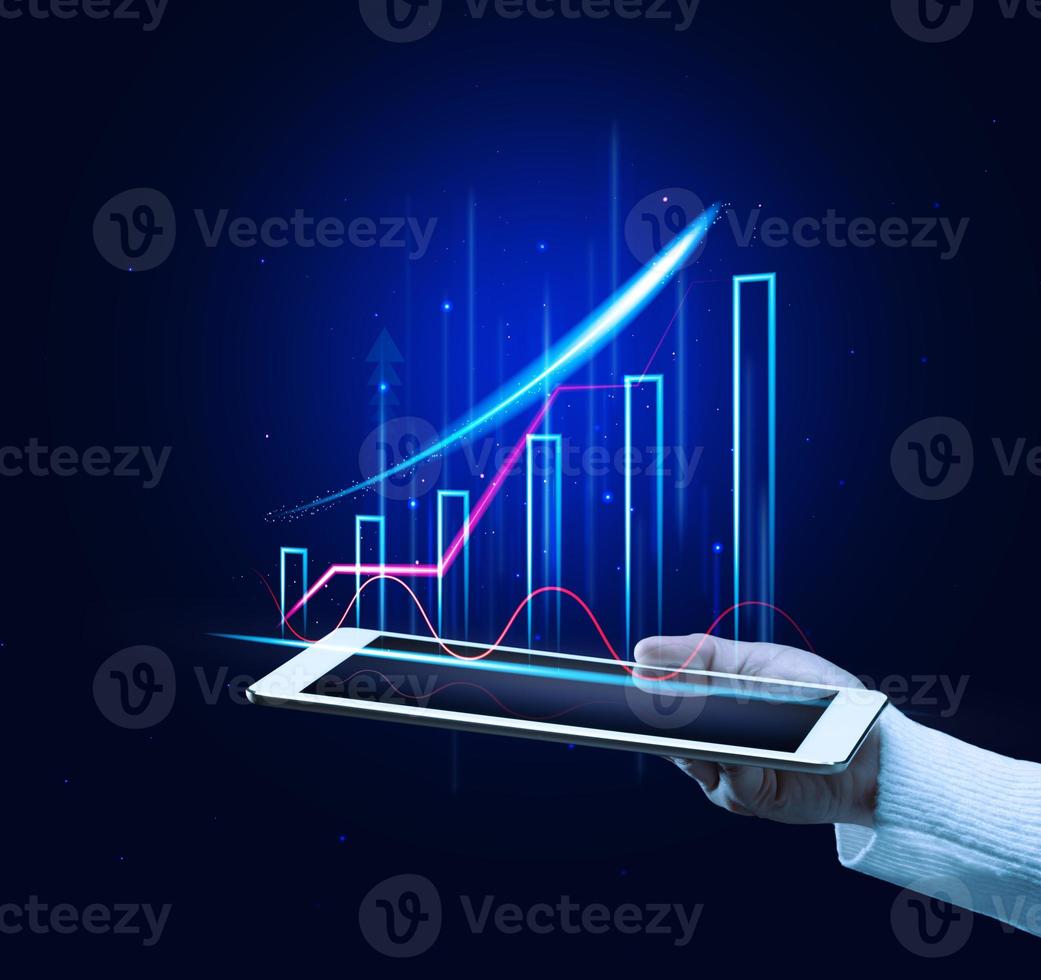 a mão de uma mulher segura um tablet com um gráfico holográfico em um fundo azul. Crescimento das vendas foto