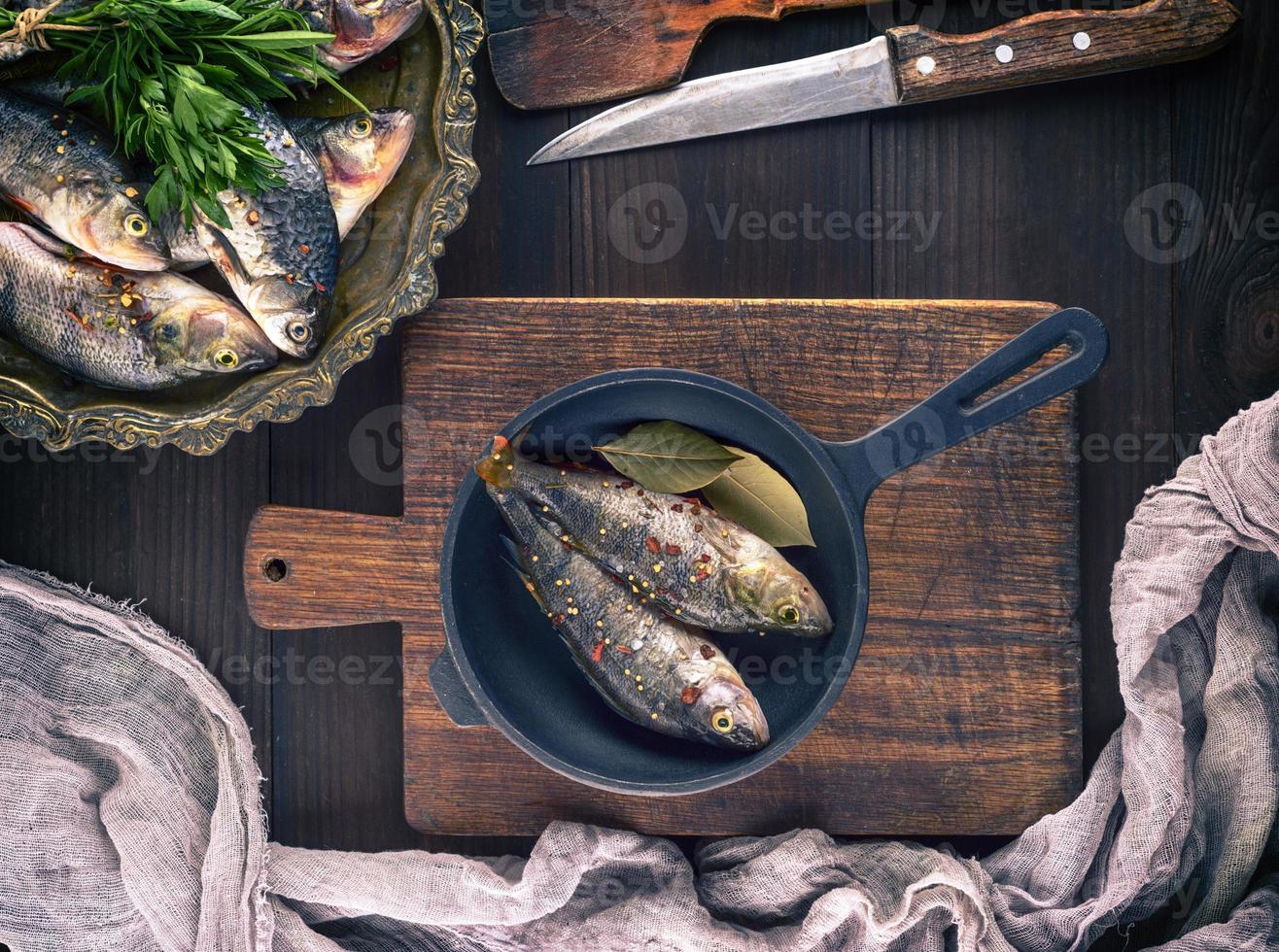 poleiro de peixe fresco com especiarias em uma frigideira preta de ferro fundido foto