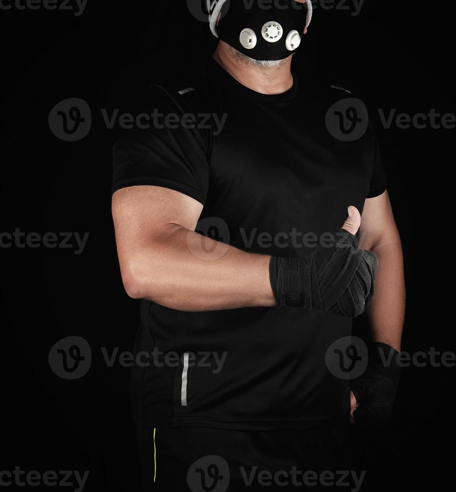 atleta de uniforme preto, máscara de treinamento e mãos envoltas em bandagens pretas foto